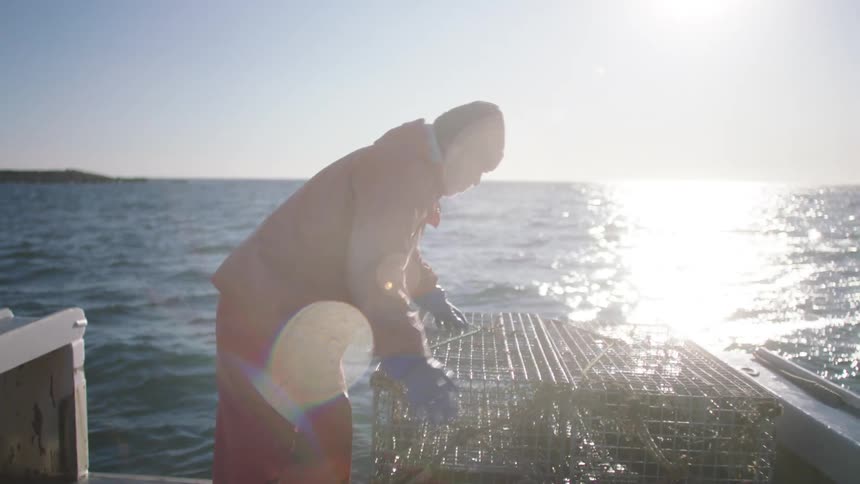 A fisherman stacks metal crates on a boat