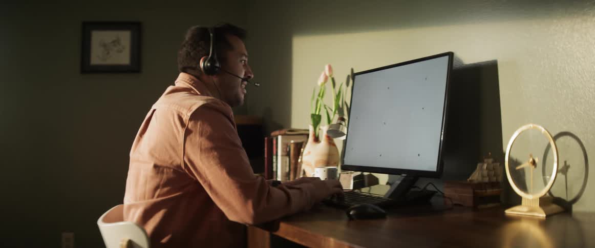 A man works at his computer while talking into a headset