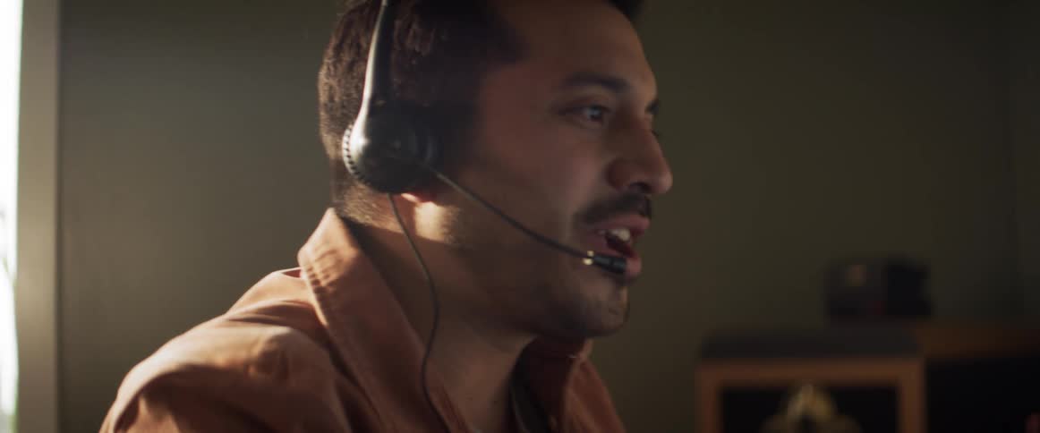 A white man talks over a computer headset while drinking out of a mug