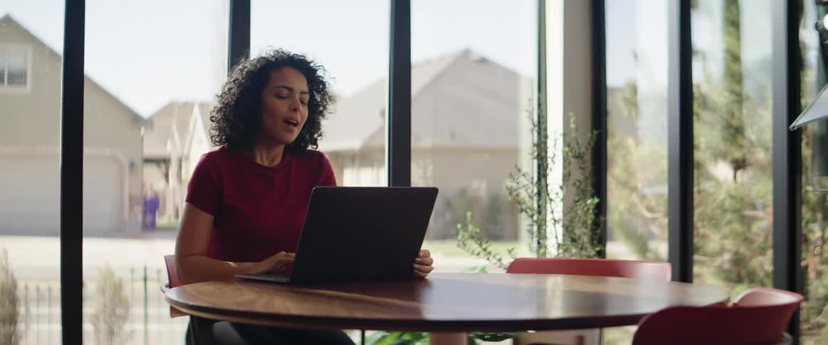 A woman sits down at a round cafeteria table with a laptop