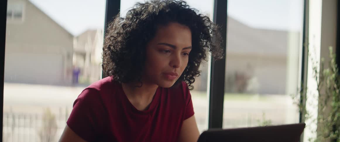 A black teenager sits down at a table and uses a laptop