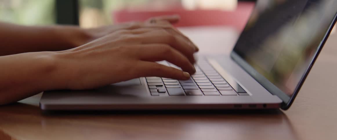 A woman sits at a table and types on her laptop