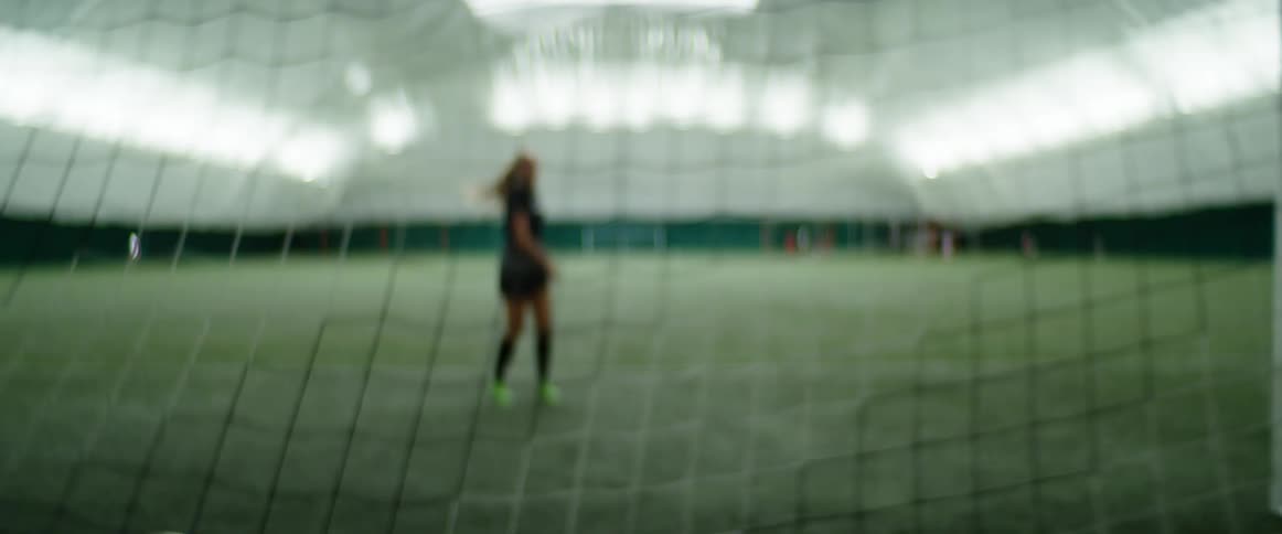A female soccer player kicks the ball into the net in a practice bubble