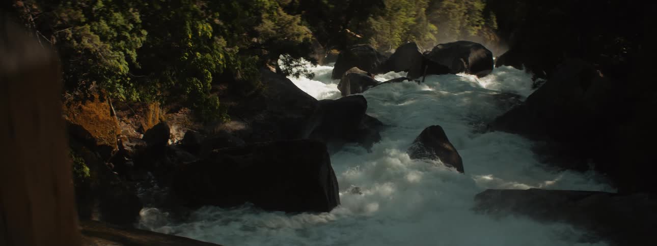 A wooden post obscures a raging river and rapids