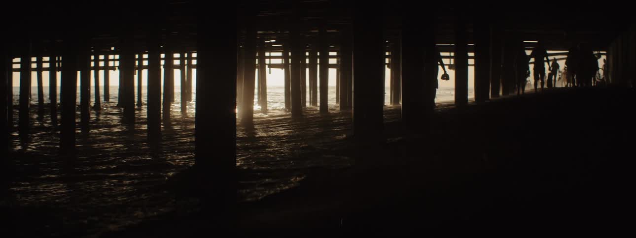 People walk under the boardwalk at sunset