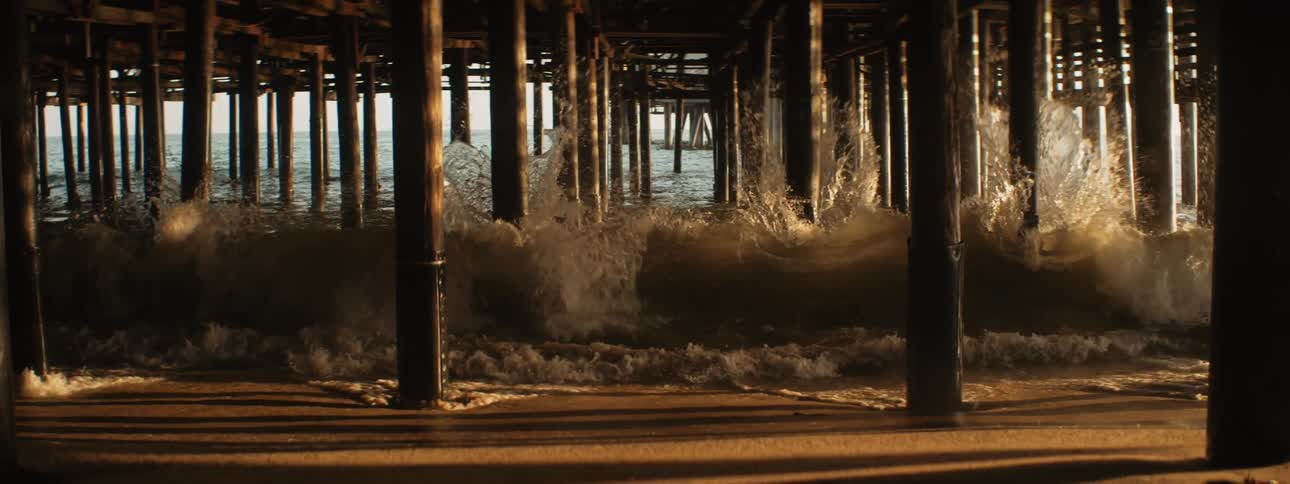 Ocean waves crash into the posts under the pier