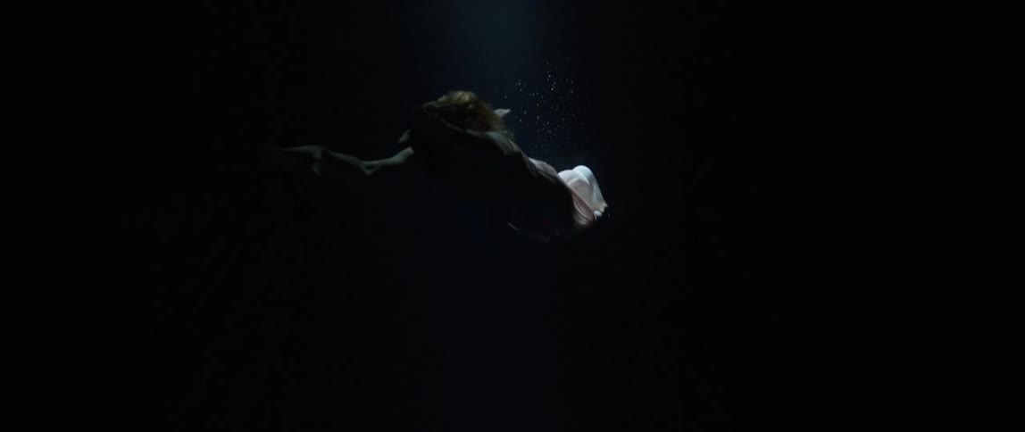 Woman undulates through dark water through light cast by spotlight