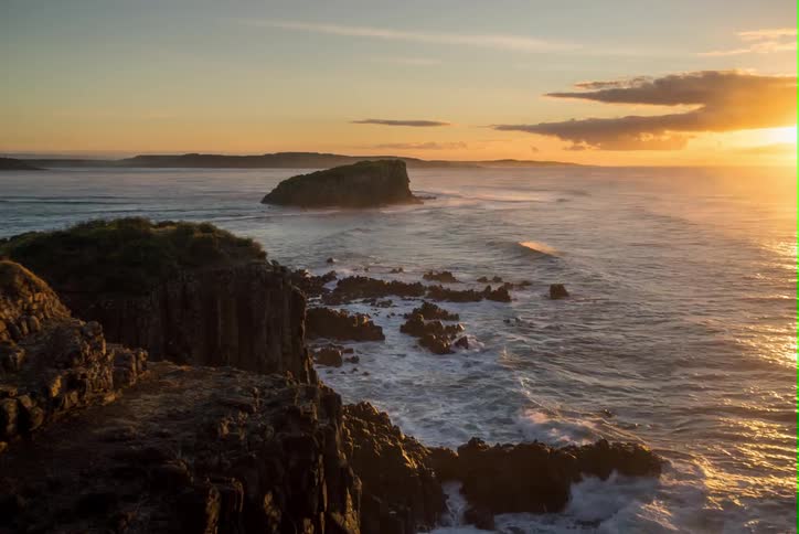 Time-lapse of waves crashing against rocky coastline s as clouds drift past the rising sun