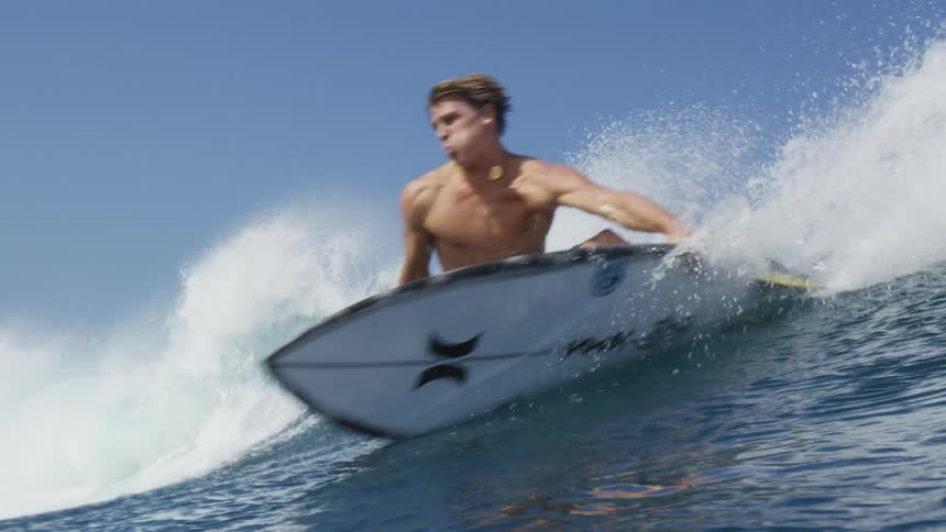 Male surfer with black swimming trunks rides on a foamy wave while standing on a surfboard
