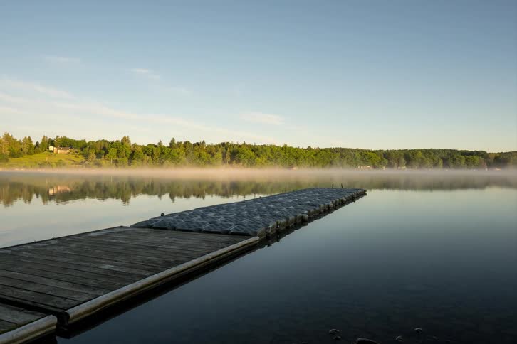 Fog rises and moves across a lake near a pier