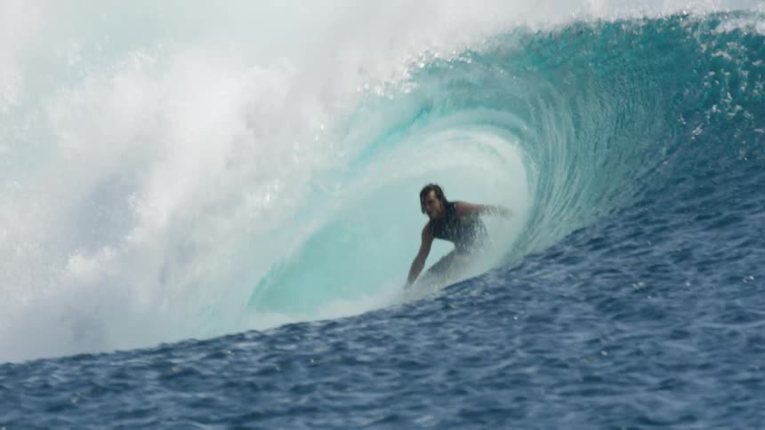 A man rides a large wave on a sunny day