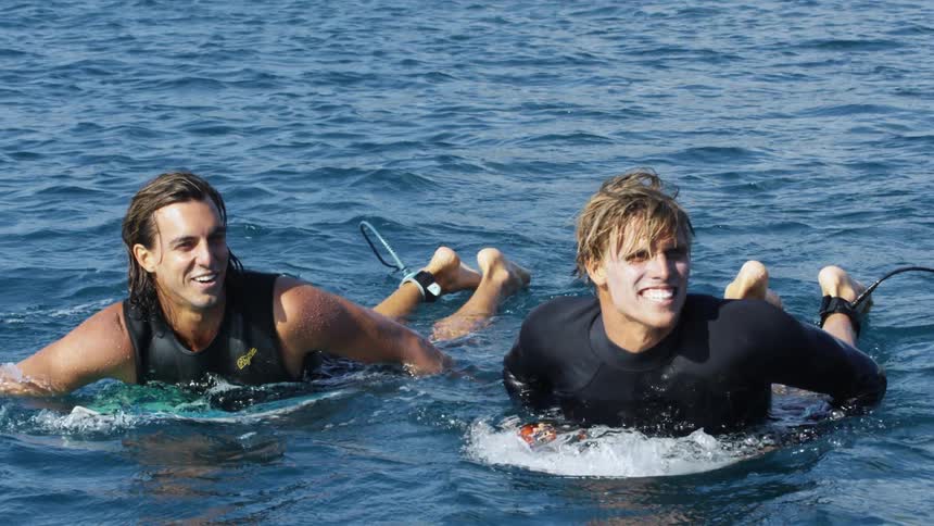 Two surfers laugh as they paddle on their boards in the ocean