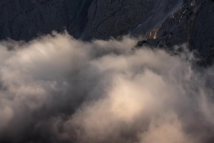 Clouds flow and swirl around a rocky mountainside