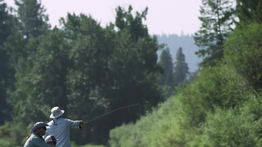 Man with a hat and blue shirt casts a fishing line by the lake