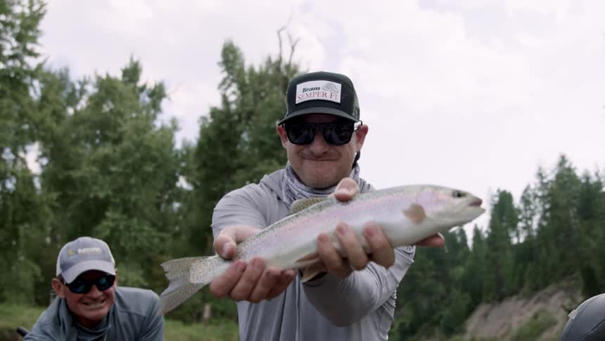 Two men wearing baseball caps and sunglasses hold a live fish on hands
