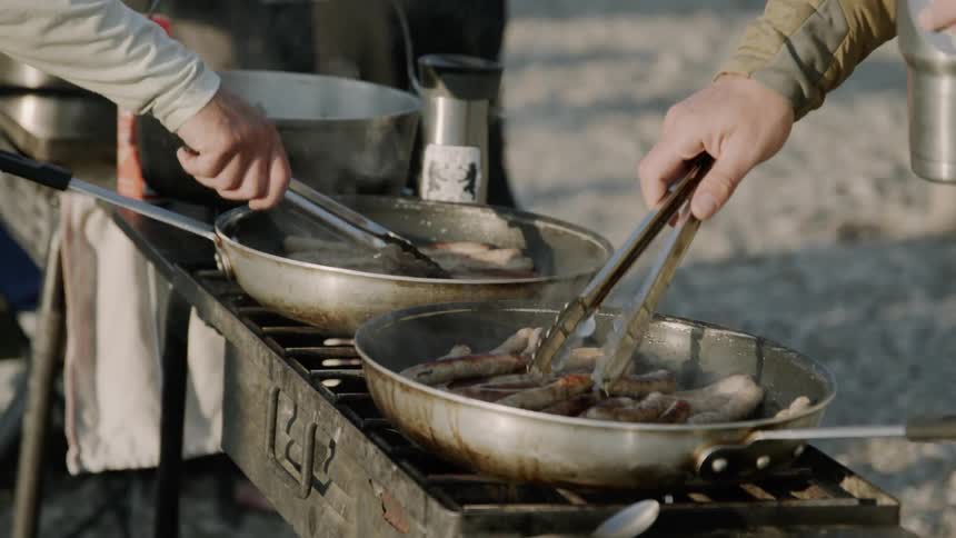 Two people cooking sausages outside