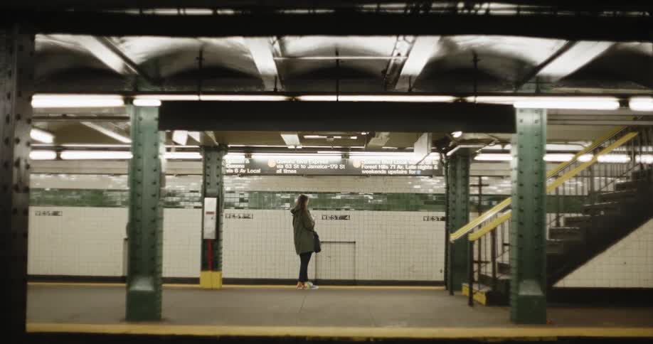 A woman stands in a train station as a man walks by