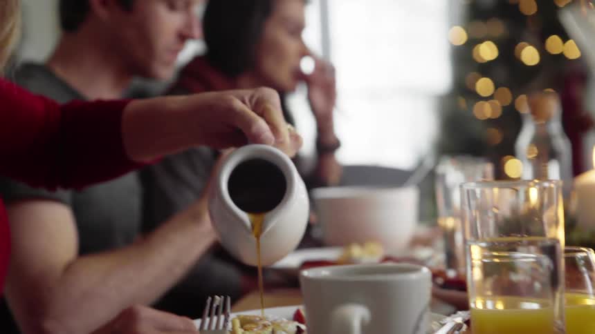 A woman pours syrup on her plate as other eat in their home