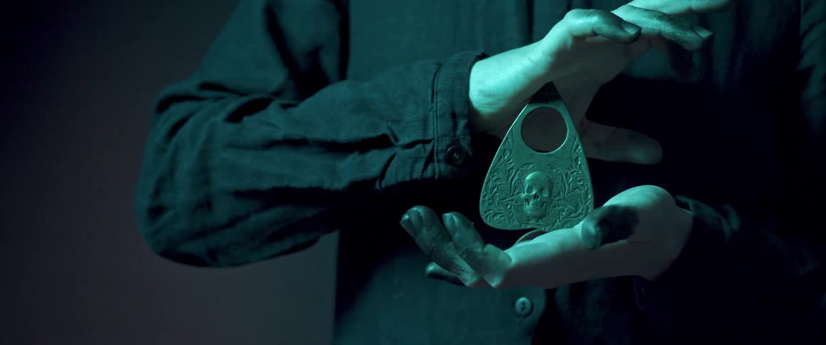 A person clasps a pointer for an ouija board