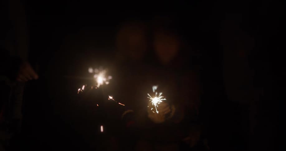A group of friends light sparklers and a large wide firework at night
