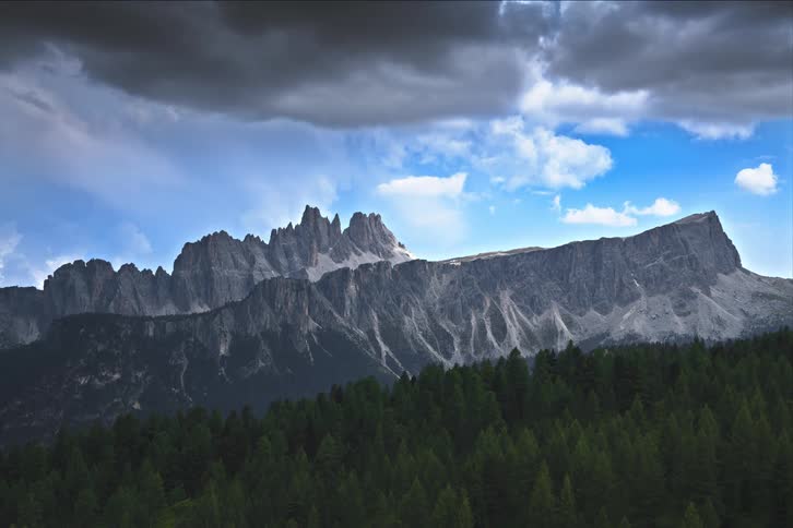 Time lapse of clouds rolling over mountain range near a pine forest