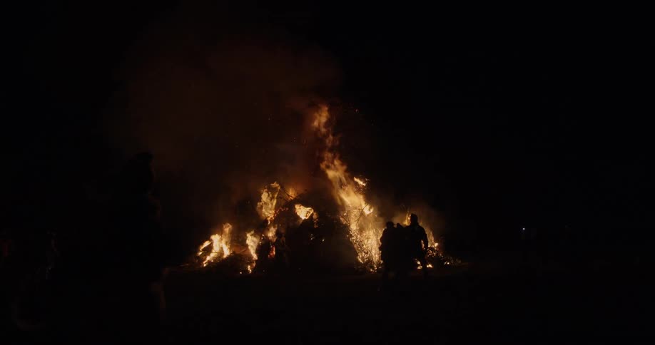 People walk away from a roaring bonfire set by people holding torches