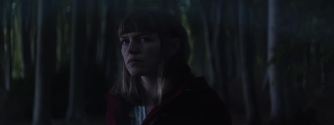 A teenager stands in a dark forest