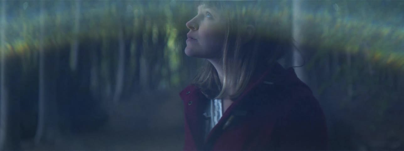 A flare descends over a womans head while she stands in a forest