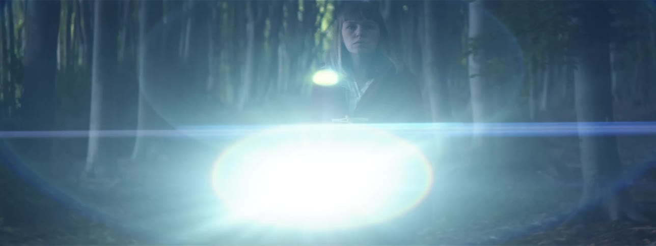 Blonde woman wearing red coat shines flashlight around surrounding woods at night
