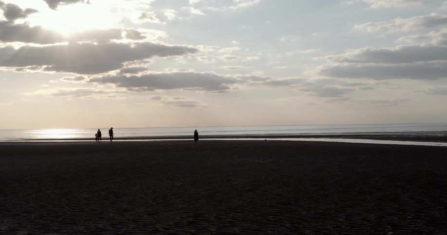Four people walking on the beach with the ocean the sky and clouds in the background
