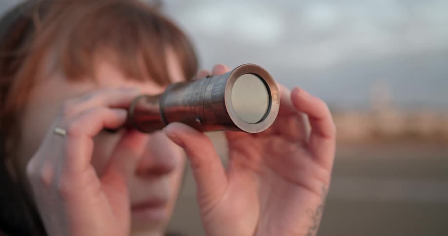 A woman uses a small handheld telescope held up to her eye while standing inparking lot