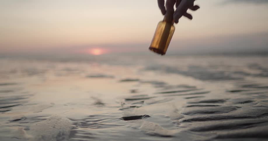 Woman picks up message in a small bottle stuck in sand at dusk