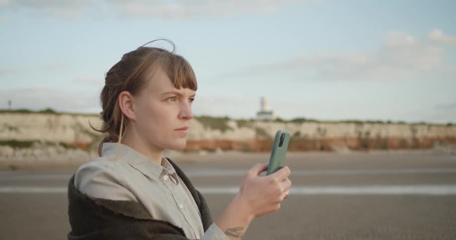 Woman on a beach takes a photo on her phone