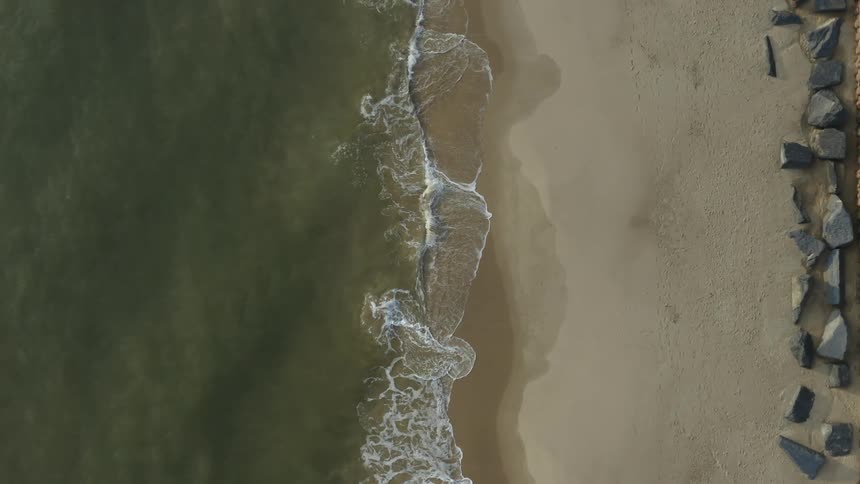 Top down aerial view of sea waves gently crashing on the sand in the shore of a beach