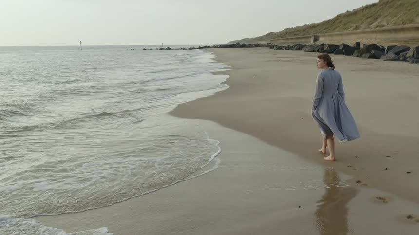 Barefoot woman walking on the sands of a beach next to the ocean at sunset