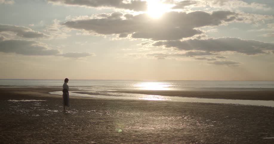 A woman stands on the beach at sunrise