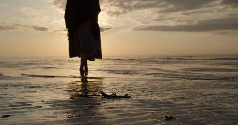 A woman slowly walks on the beach with keys in the foreground