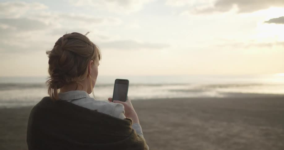 Woman standing on the beach takes a photo with her phone