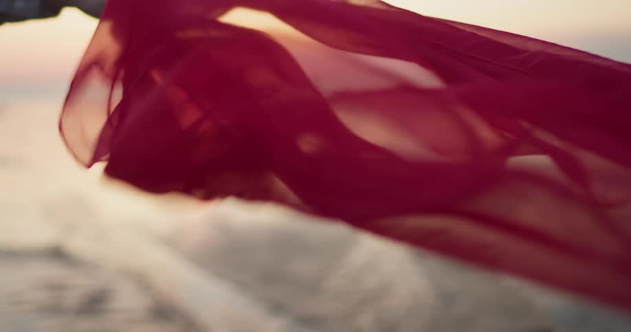 A person holding a sheer red fabric as it flutters in the wind
