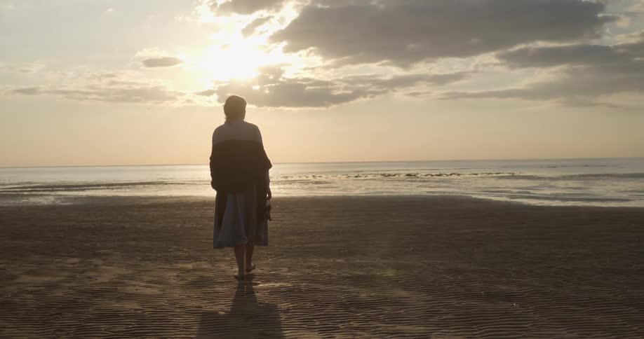 Woman with a dress walks barefoot on the beach at sunset next to the sea