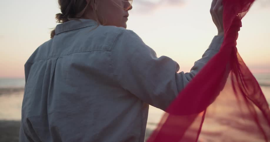 A woman holds a red scarf as she walks on the beach