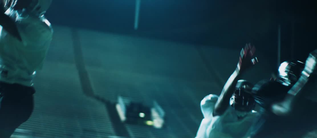 A football player runs past a pair of opposing players to catch a thrown football in an empty football stadium at night