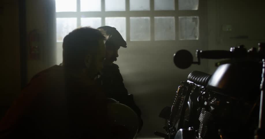 Two men bend down to look at a motorcycle