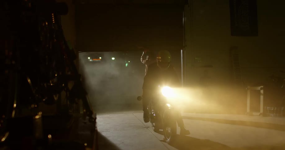 A man drives a motorcycle in to a garage and another man closes the door