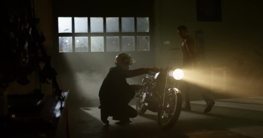 Two men inspect a motorcycle in a garage