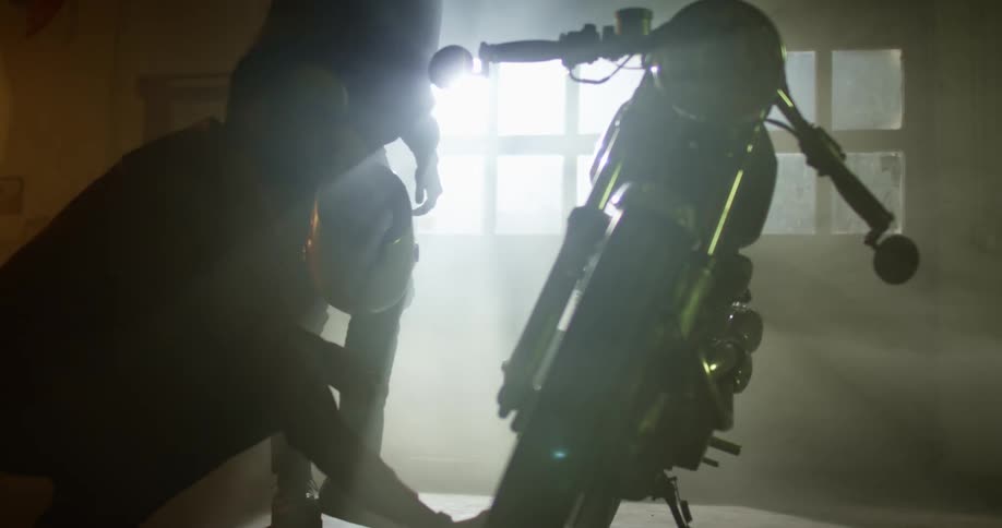 Two men check up a motorcycle on a dimly lit workshop