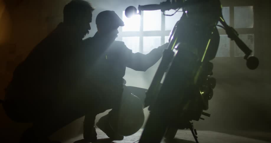 Two men stooping down looking at a motorcycle in a garage