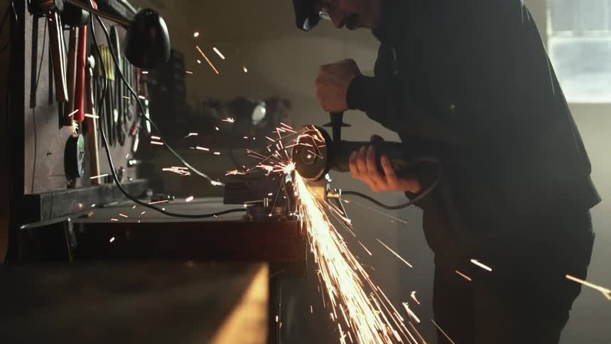 A man uses a power tool at his workbench in his garage causing sparks to fly