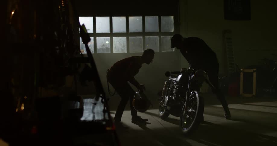 Two men in a garage look at a motorcycle