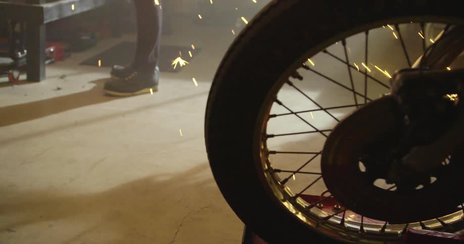 A motorcycle wheel with a person standing and sparks falling in the background